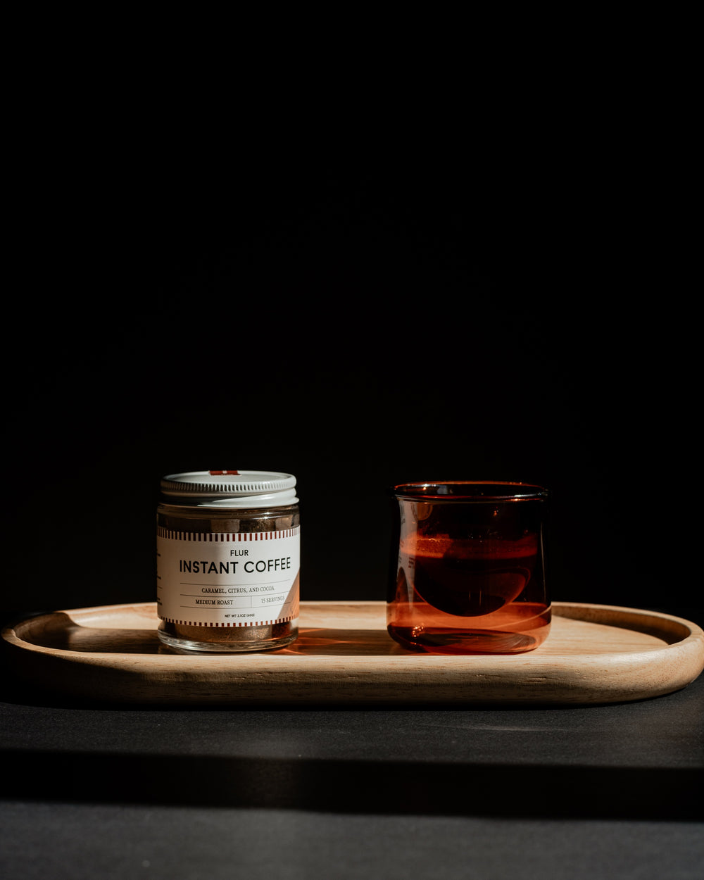 FLUR Instant Coffee jar and amber glass on a wooden tray